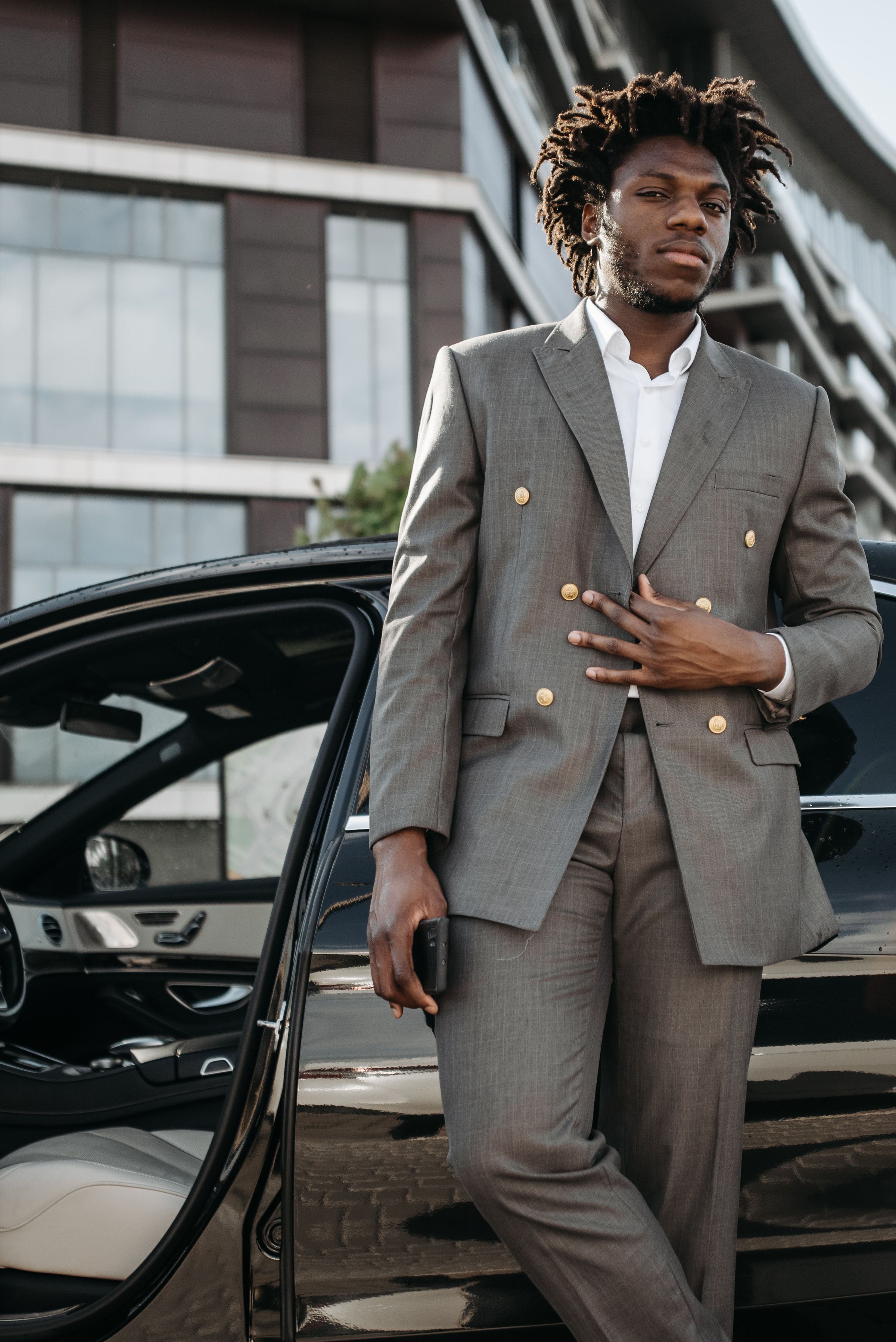 A suited close-protection professional maintains an alert presence beside a secured vehicle.
